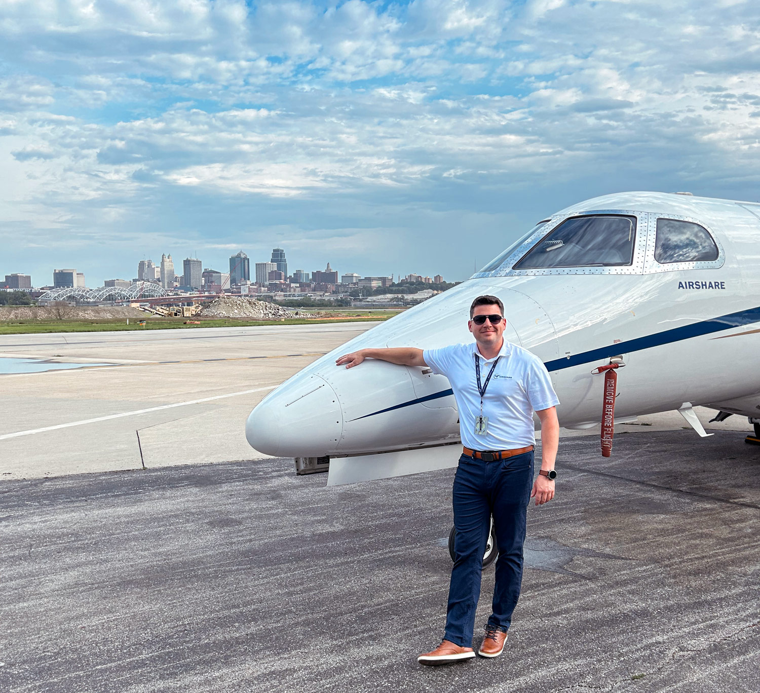 Steve Wynne, standing at the nose of an Airshare Phenom 300 in front of a city skyline.