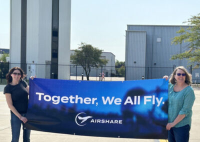 Airshare employees, Heather W. and Deanna W. in Waukegan holding am Airshare branded banner outside.