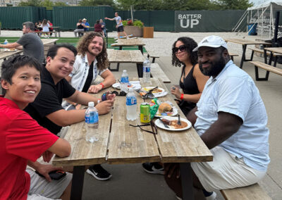 Airshare employees, Alexandro Paredes and Taylor Kelly with their guests enjoying food at a picnic table the the Monarchs game.
