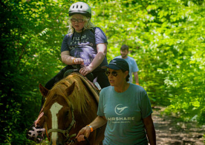Camper riding a horse, led by employee Kate Gruell.