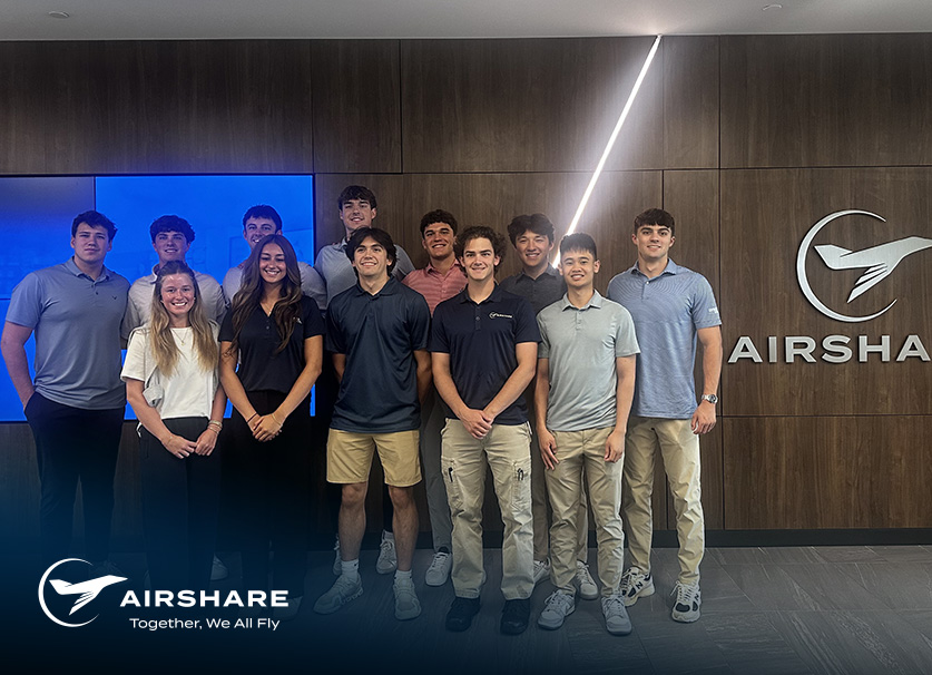 Group of Interns gathered in front of wooden wall with Airshare signage posed for group photo.