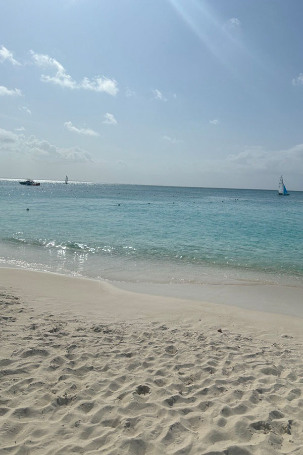White sand beach and clear turquoise water in Turks & Caicos with sailboats visible offshore.